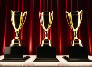 Eleganta ceremonie de premiere: scenă cu lumini sclipitoare, trofee abstracte pe piedestale, atmosferă festivă într-un salon de bal luxos al unui hotel. Iluminare cinematografică, 8k, hiper-realist.